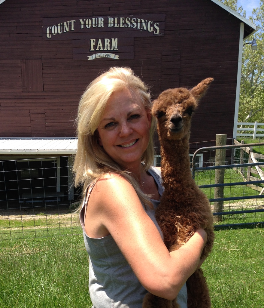 Annette holding a cria in front of Count Your Blessings Farm barn